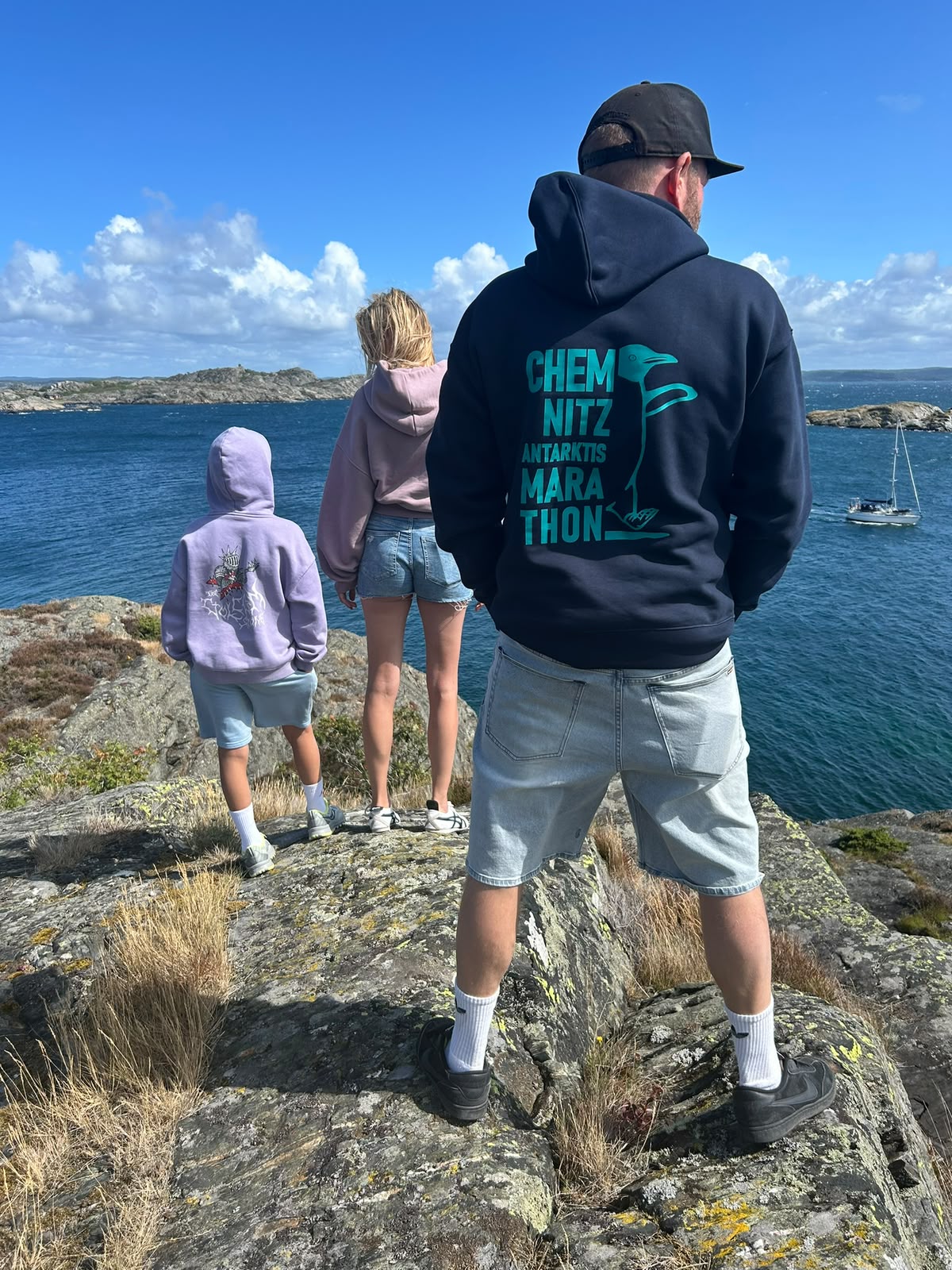 Person am Wasser von hinten, trägt den dunkelblauen Hoodie mit dem türkisfarbenen Rückendruck